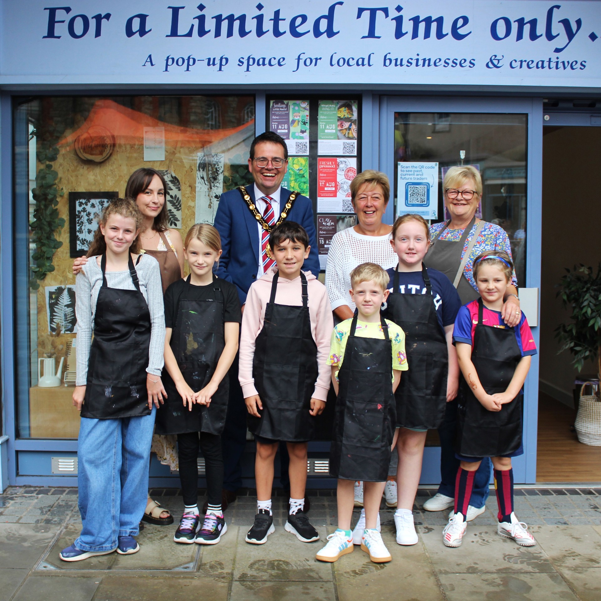 Councillor Huw David, Mayor of Bridgend County Borough Council and Carly Lewis, owner of Nature’s Printmaker outside of the pop-up unit in Maesteg Market with the children and parents who attended the dinosaur themed printing workshop.