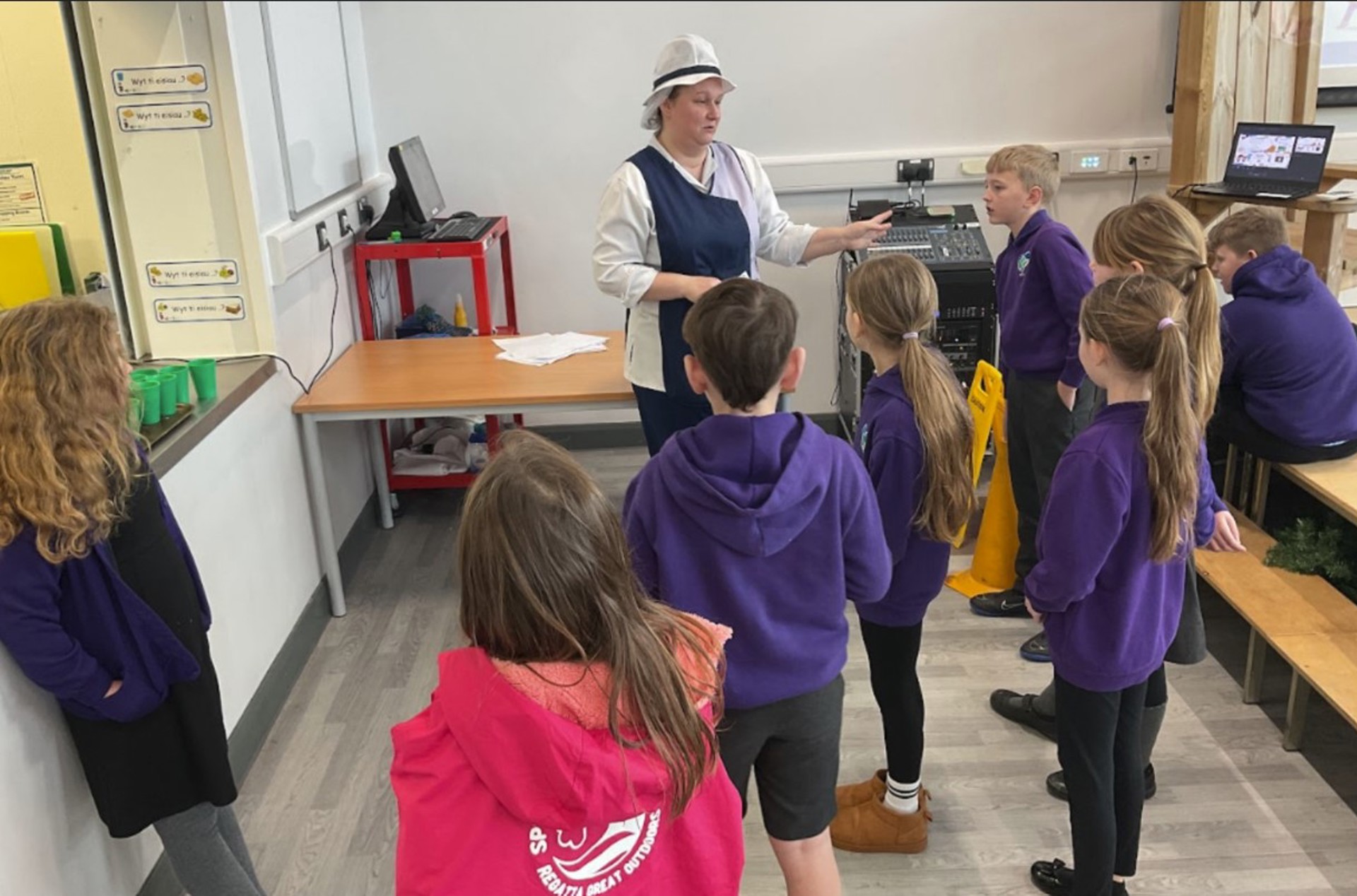Pupils interviewing kitchen staff about Welsh phrases that may help them when serving the children food.