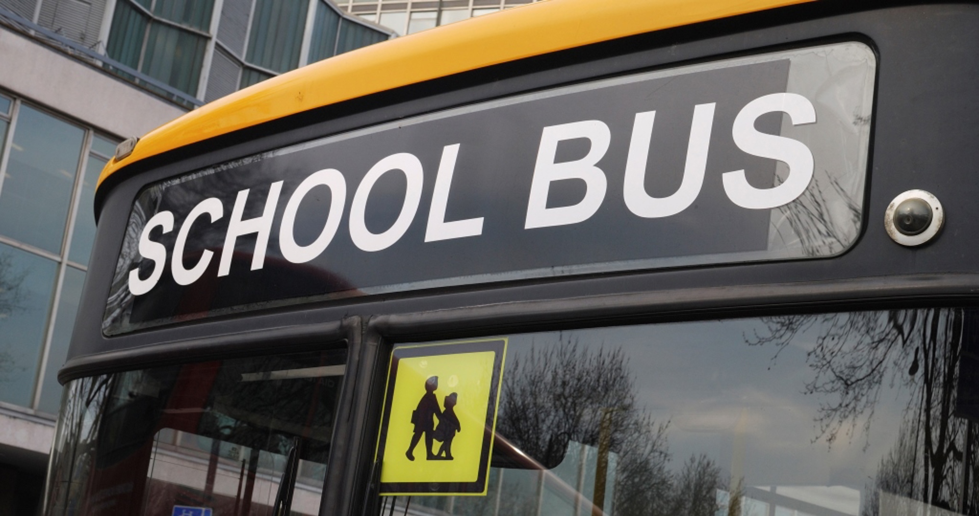 The top part of the front of a school bus with a prominent ‘school bus’ sign, and a warning icon to note that children use the vehicle.