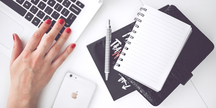 A notebook, a mobile phone and a laptop on a desk.